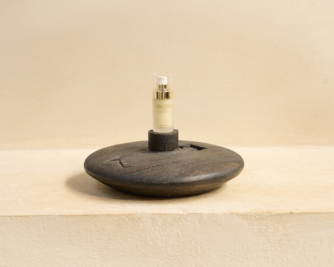 Skincare bottle of Ablooms Supreme Skin Elixer on a dark wooden stand against a beige background